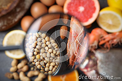 Different products with magnifier focused on soy beans and shrimps. Food allergy concept Stock Photo