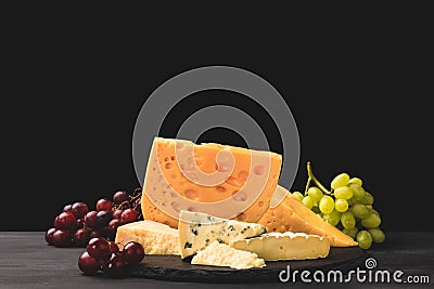 Different types of cheese on board with grapes on black Stock Photo