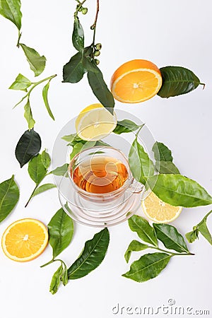 Different types of fresh raw green tea leaf flower bud dropping floating elevated lemon orange slice over transparent glass teacup Stock Photo