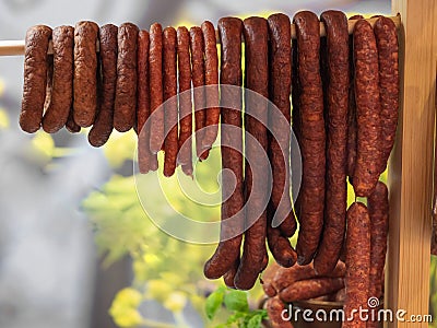 Different types of homemade smoked dry sausages hanging on a dark wooden background. Assortment of delicious deli meats, Salami Stock Photo