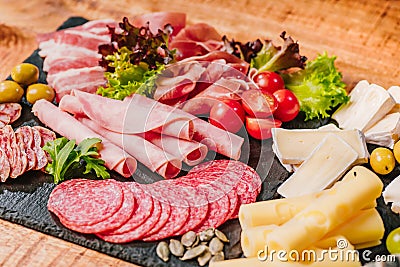 Different types of sausages with cheese on wooden table.Cold cuts of different types of sausages on a black flat plate on a wooden Stock Photo