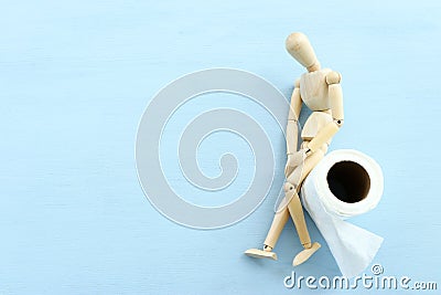 digestion or constipation health problen. Wooden figure sit on a roll of toilet paper. blue background Stock Photo