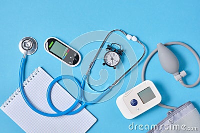 Digital blood pressure monitor, glucometer, stethoscope, notepad and alarm clock on blue background top view Stock Photo