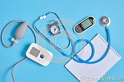 Digital blood pressure monitor, glucometer, stethoscope, notepad and alarm clock on blue background top view Stock Photo