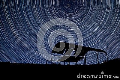 Digital composite image of star trails around Polaris with derelict barn silhouette Stock Photo