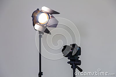 Digital SLR camera and a spotlight with a Fresnel lens on a gray background. Shooting in the interior Stock Photo