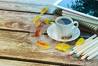 Digital tablet, books, colorfull pencils and cup of coffee on old wooden table outdoor in the park. Stock Photo
