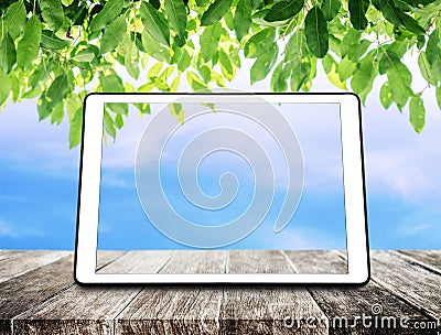 Digital tablet on wooden table with green leaves and blue sky background Stock Photo