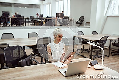 Digital technologies at work. Young, beautiful tattooed business lady in eyewear using digital tablet and smiling Stock Photo