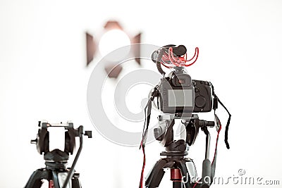 A digital video camera with a microphone on a tripod on a white background, a bright spotlight in the background Stock Photo