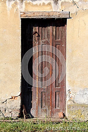 Dilapidated old wooden entrance doors with rusted metal frame mounted on cracked light yellow abandoned family house wall Stock Photo