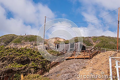 Dilapidated small building on hill with wooden staircase leading to it. Blue sky with puffy clouds Stock Photo