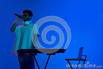 Dimly lit club scene with young DJ energizing the crowd with infectious music against blue background in neon light Stock Photo