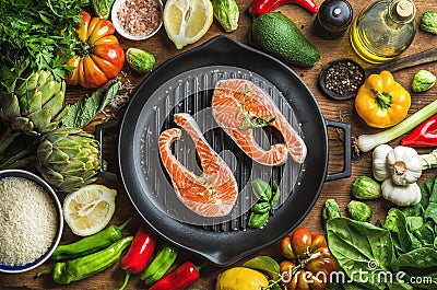 Dinner cooking ingredints. Raw uncooked salmon fish with vegetables, rice, herbs, spices and oil in iron grilling pan Stock Photo