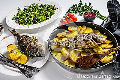 Dinner with grilled sea bream fish, arugula salad with tomatoes, baked potatoes. White background. top view Stock Photo