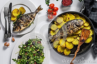 Dinner with grilled sea bream fish, arugula salad with tomatoes, baked potatoes. White background. top view Stock Photo