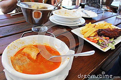 Dinner at restaurant - Hungarian fish soup named halaszle and fried hake with French fries and vegetables Stock Photo