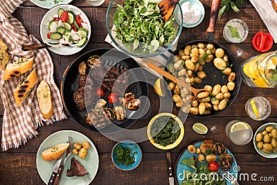 Dinner table with grilled steak, vegetables, potatoes, salad, sn Stock Photo