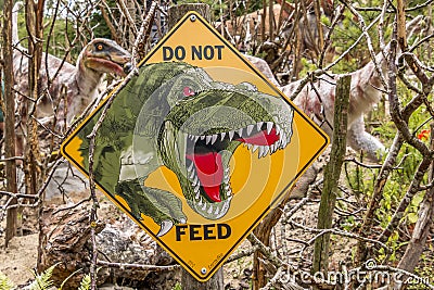 Dinosaurs fighting for some food, in the foreground a yellow that says you must not feed the dinosaurs Editorial Stock Photo