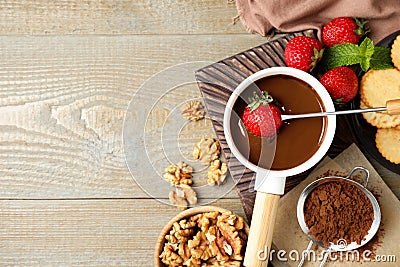 Dipping strawberry into fondue pot with milk chocolate on wooden table, flat lay Stock Photo