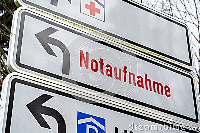 Direction sign shows the Red Cross and German text Notaufnahme, meaning emergency department, at the driveway to a large hospital Editorial Stock Photo