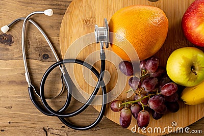 Directly above shot of apples with orange and grapes on wooden tray by stethoscope on table Stock Photo