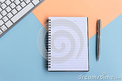 Directly above view of simple office desk with computer keyboard, note pad and pen on multi colored background Stock Photo