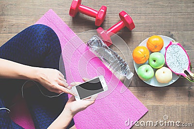 Directly above of woman in fitness clothing using mobile phone with sport equipments and fruits on the floor, Healthy Stock Photo