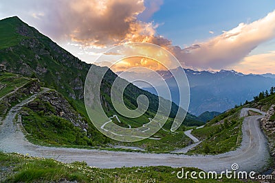 Dirt mountain road leading to high mountain pass in Italy Colle delle Finestre. Expasive view at sunset, colorful dramatic sky, Stock Photo