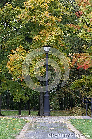 A dirt path in the park and a vintage lantern. The trees show colorful autumn leaves Stock Photo