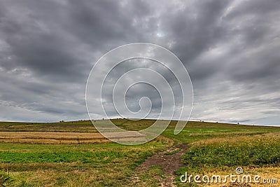 Dirt road leading to the top of a green hill at summertime, gathering storm clouds Stock Photo