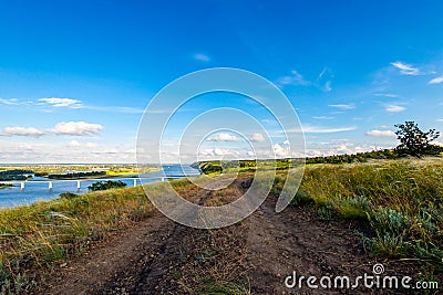 Dirt road in the steppe between feather fields grass and parallel with river Stock Photo