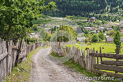 Dirt road up the slope along the wooden fences, in the upper part of Mestia. Svaneti Region, Georgia Stock Photo