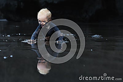 Dirty child crawling on wet black sand beach Stock Photo