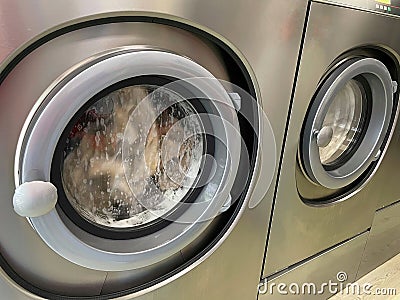 Dirty clothes spinning inside the main doors of two stainless steel industrial washing machines Stock Photo
