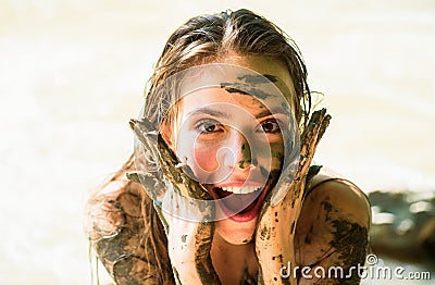 Dirty female model. Woman in clay mask laughs. Crazy girl in medical mud. Spa Outdoor. Happy dirty woman in Dead sea Stock Photo
