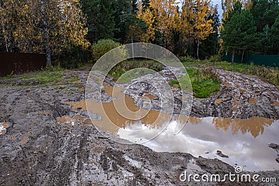 Dirty forest road with a large muddy puddle and reflected clouds Stock Photo