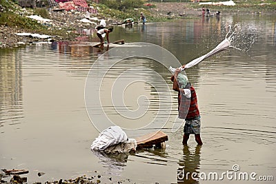 Dirty Laundry: Washerman wash clothes in polluted water Editorial Stock Photo