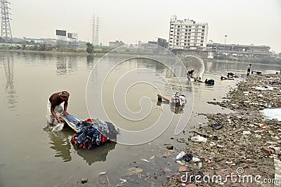 Dirty Laundry: Washerman wash clothes in polluted water Editorial Stock Photo