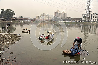 Dirty Laundry: Washerman wash clothes in polluted water Editorial Stock Photo