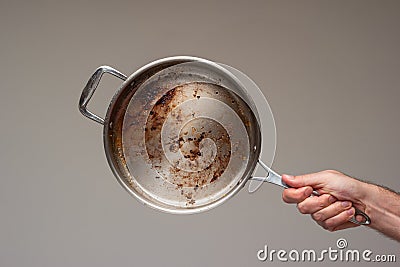Dirty oily burnt metal frying pan held in hand by male hand Stock Photo