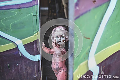 Dirty plastic baby doll standing by the door at the metal shop looking eerie and hunted weaving Stock Photo