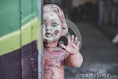 Dirty plastic baby doll standing by the door at the metal shop looking eerie and hunted weaving closeup Stock Photo