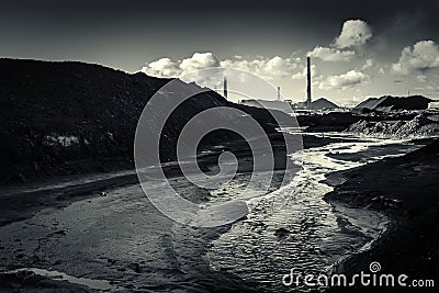 Dirty river water after factory waste with piles of black waste on the background of pipes and factory workshops Stock Photo