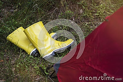 Dirty yellow rubber boots with a white border lie on the wet grass near the tent in a tourist camp Stock Photo