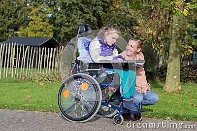 A disabled girl in a wheelchair outside with a care assistant Stock Photo