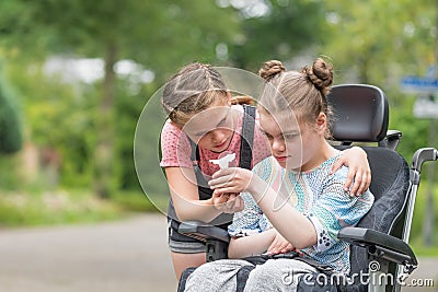 Disability a disabled child in a wheelchair relaxing outside with her sister Stock Photo