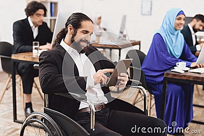 Disabled arab man in wheelchair working in office. Man is talking on tablet. Stock Photo