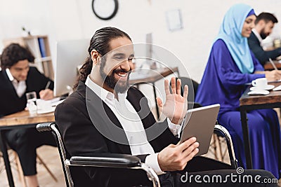 Disabled arab man in wheelchair working in office. Man is talking on tablet. Stock Photo