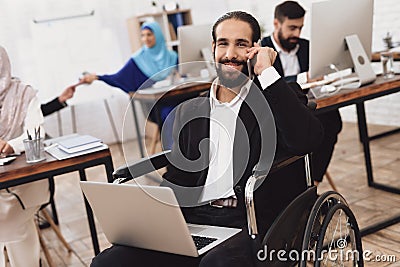 Disabled arab man in wheelchair working in office. Man is working on laptop. Stock Photo